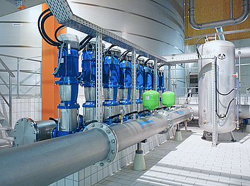 Industrieller Edelstahltank mit Ozonanlage, blauer Kreiselpumpe und Rohrleitungen auf konischen Maschinenfüßen.