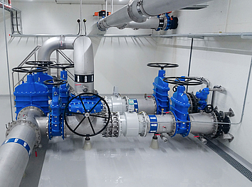 Industrielle Wasserfiltrationsanlage mit Membranmodulen, Edelstahlrohren und blauer Hochdruckpumpe auf Riffelblech.